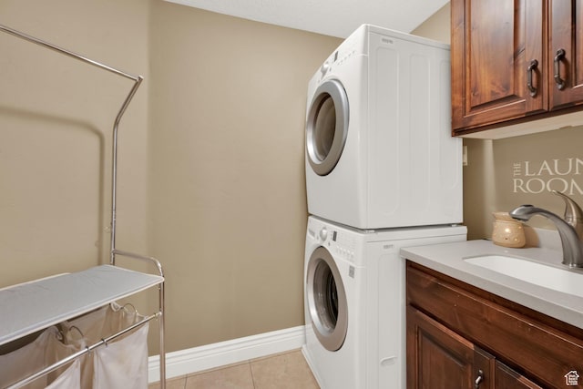 laundry area featuring light tile patterned floors, baseboards, a sink, stacked washer and dryer, and cabinet space