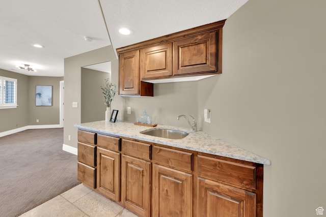 kitchen with baseboards, a sink, brown cabinets, light stone counters, and light carpet