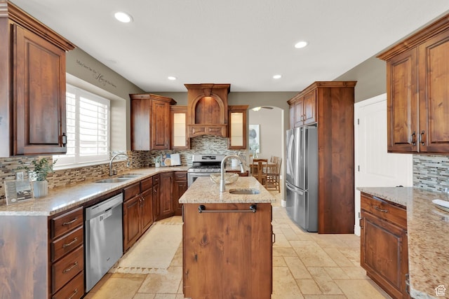 kitchen with tasteful backsplash, a sink, premium range hood, a center island with sink, and stainless steel appliances