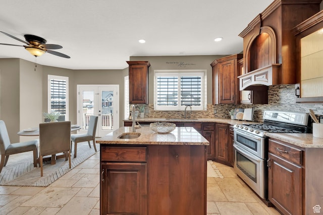 kitchen with stone tile flooring, a kitchen island with sink, ceiling fan, double oven range, and decorative backsplash
