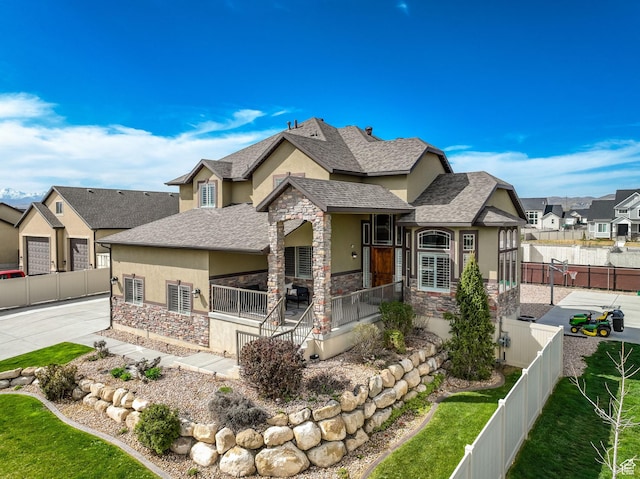 craftsman-style home with stone siding, a fenced backyard, stucco siding, a residential view, and roof with shingles