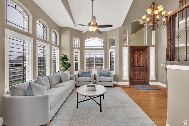 living room with a high ceiling, wood finished floors, ceiling fan with notable chandelier, and baseboards