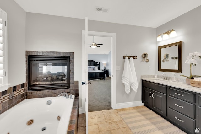 full bath featuring a jetted tub, vanity, a multi sided fireplace, a ceiling fan, and visible vents