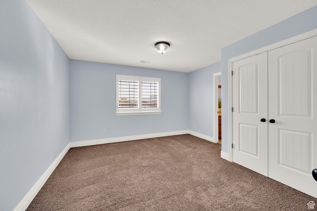 unfurnished bedroom featuring a closet, dark colored carpet, and baseboards