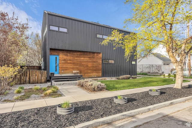 modern home featuring board and batten siding, a front lawn, fence, and an outdoor structure