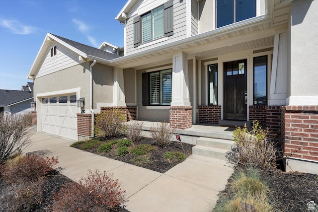 view of exterior entry featuring covered porch, stucco siding, brick siding, a garage, and concrete driveway