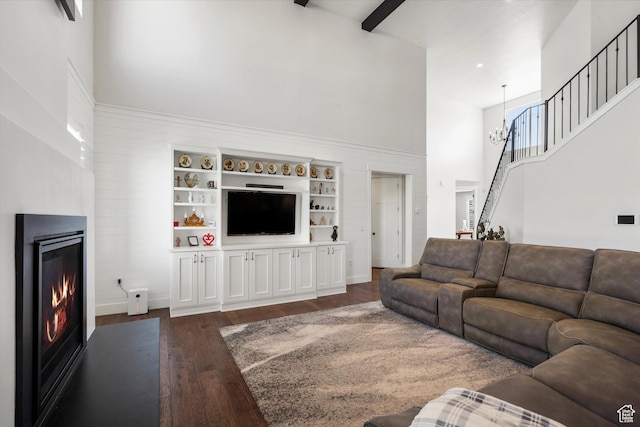 living room with dark wood finished floors, a towering ceiling, a glass covered fireplace, stairway, and a chandelier