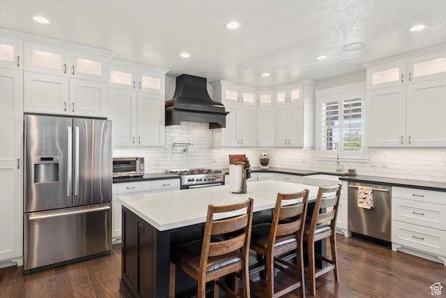 kitchen featuring custom exhaust hood, decorative backsplash, dark wood finished floors, and appliances with stainless steel finishes