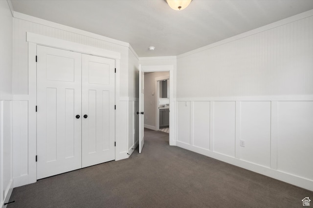 unfurnished bedroom featuring a decorative wall, a closet, a wainscoted wall, and carpet floors