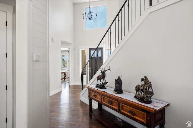 foyer entrance featuring a towering ceiling, dark wood-style flooring, stairs, a notable chandelier, and baseboards