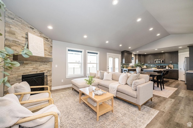 living room with baseboards, a stone fireplace, light wood-type flooring, vaulted ceiling, and recessed lighting