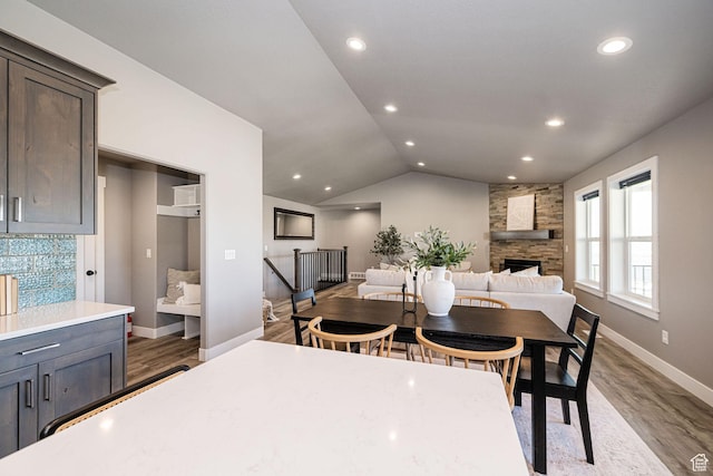 dining area with baseboards, a stone fireplace, recessed lighting, wood finished floors, and lofted ceiling