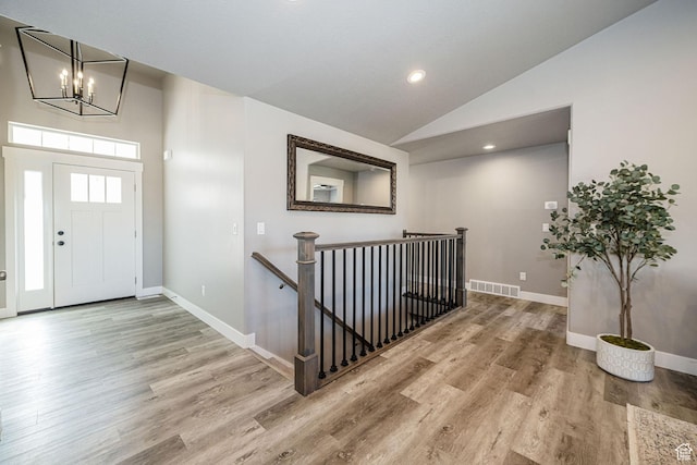 entryway featuring baseboards, a chandelier, light wood-style flooring, visible vents, and high vaulted ceiling