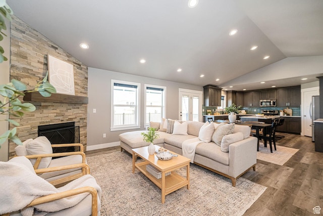 living area featuring a stone fireplace, recessed lighting, wood finished floors, and vaulted ceiling