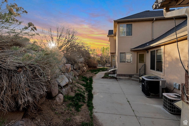 property exterior at dusk with stucco siding, a patio, and cooling unit