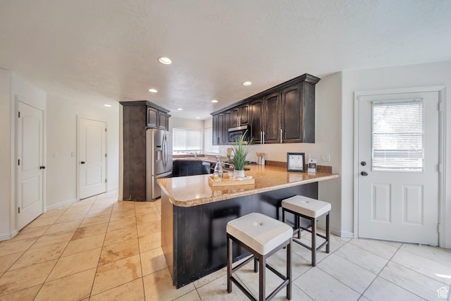 kitchen featuring light countertops, light tile patterned floors, dark brown cabinetry, a peninsula, and appliances with stainless steel finishes