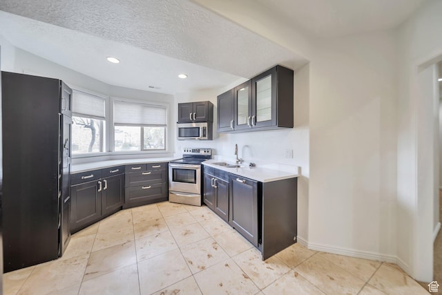 kitchen featuring stainless steel appliances, a textured ceiling, recessed lighting, glass insert cabinets, and light countertops
