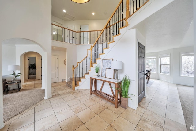 foyer featuring arched walkways, baseboards, a high ceiling, stairs, and light tile patterned floors