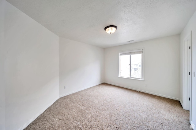 unfurnished room with a textured ceiling, carpet flooring, baseboards, and visible vents