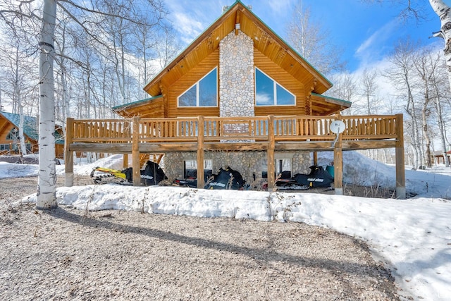 snow covered property with log exterior, stone siding, and a wooden deck