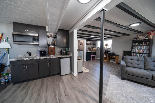 bar featuring dishwashing machine, light wood-type flooring, stainless steel microwave, a sink, and baseboards