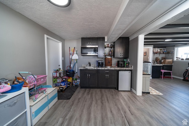 bar with wet bar, a textured ceiling, stainless steel microwave, light wood finished floors, and refrigerator