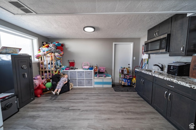 kitchen featuring light wood-type flooring, visible vents, stainless steel microwave, a sink, and dark cabinetry