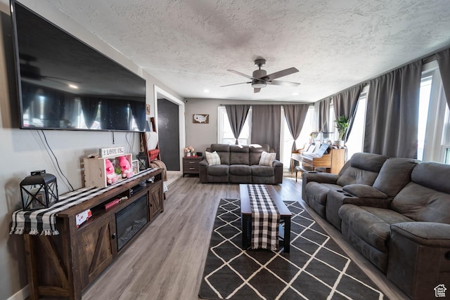 living room featuring a ceiling fan, baseboards, light wood finished floors, and a textured ceiling