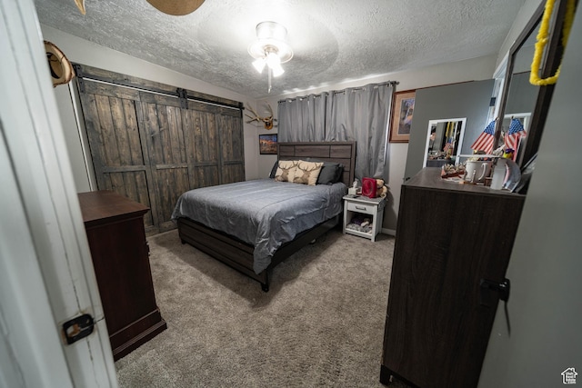 bedroom with a barn door, carpet, and a textured ceiling
