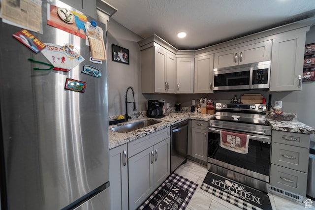 kitchen featuring light stone counters, a sink, gray cabinetry, and stainless steel appliances