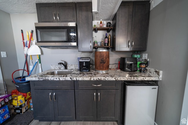 kitchen featuring a sink, stainless steel microwave, open shelves, and a textured ceiling