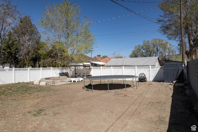 view of yard featuring a storage shed, a fenced backyard, a trampoline, and an outbuilding