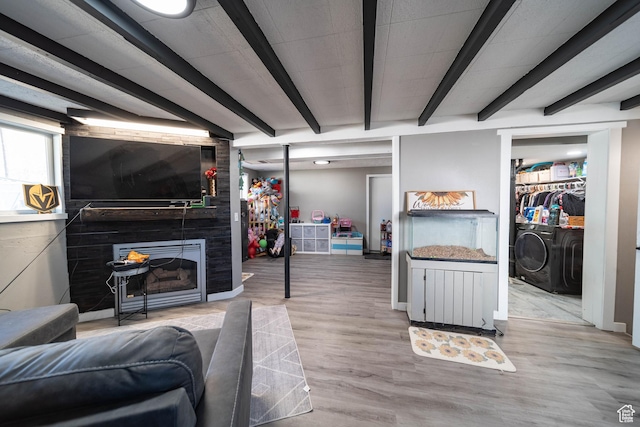 living room featuring separate washer and dryer, a large fireplace, baseboards, beam ceiling, and wood finished floors