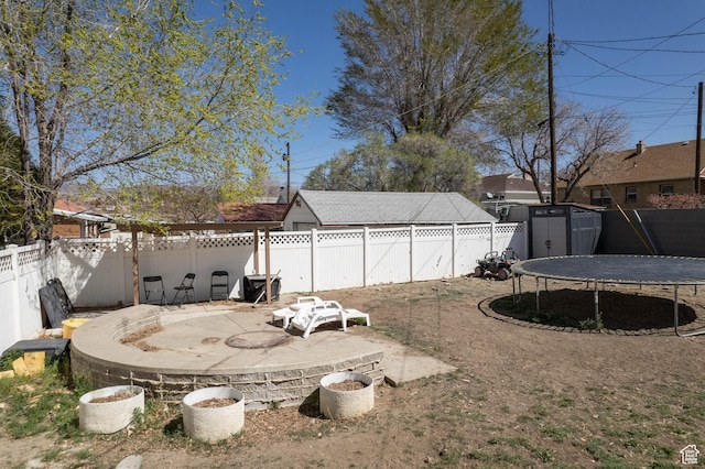 view of yard featuring a patio area, a trampoline, a fenced backyard, a storage unit, and an outbuilding