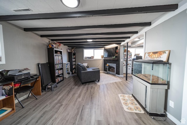 living area with a fireplace, visible vents, light wood-type flooring, and beamed ceiling