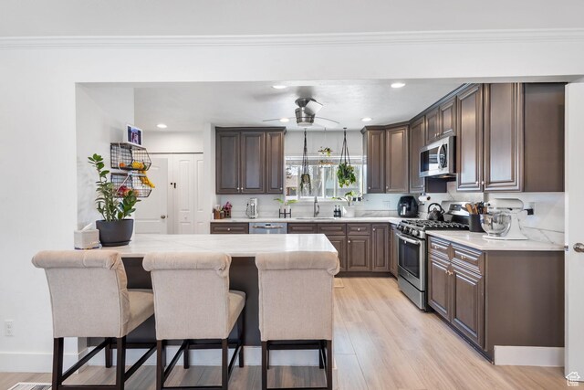 kitchen featuring light wood-type flooring, light countertops, dark brown cabinets, a breakfast bar area, and stainless steel appliances