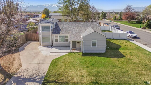 view of front facade featuring a front yard, a mountain view, a shingled roof, a patio area, and a fenced backyard