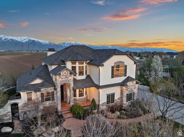 french country home with a mountain view, stone siding, a chimney, fence, and stucco siding