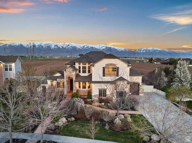 french country inspired facade with fence, stucco siding, stone siding, and a mountain view