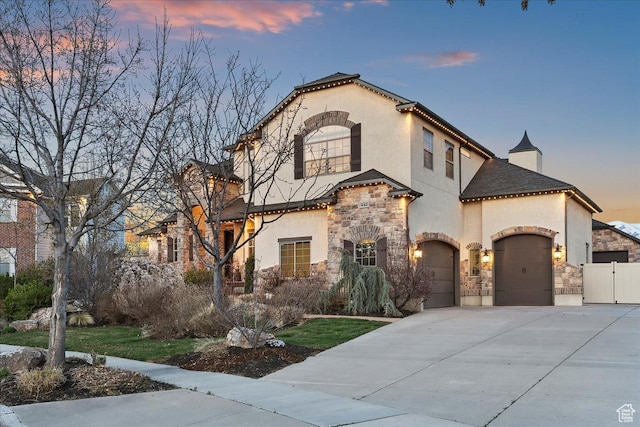 mediterranean / spanish-style home featuring a garage, stucco siding, fence, stone siding, and driveway