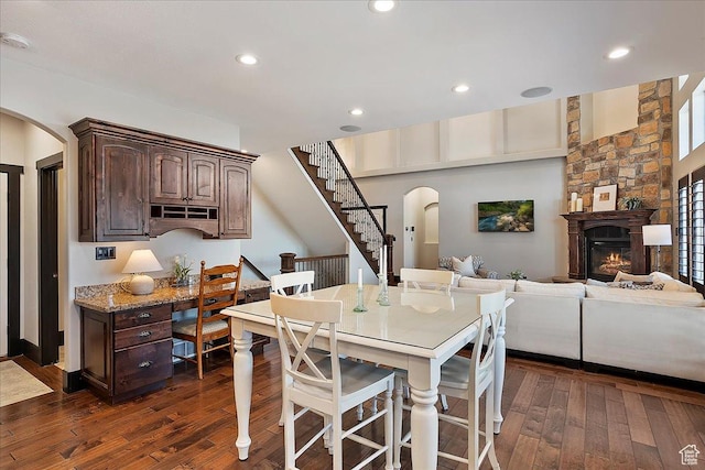 dining area featuring a large fireplace, recessed lighting, arched walkways, and dark wood-style floors