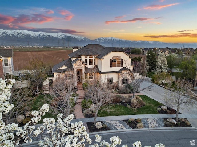 french country style house with a mountain view, stone siding, driveway, and stucco siding