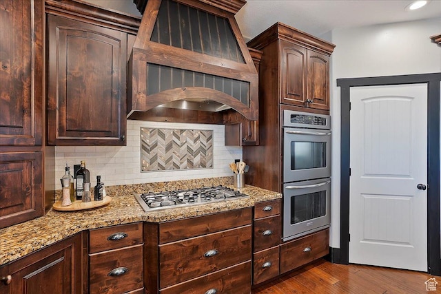 kitchen featuring custom range hood, backsplash, light stone countertops, and stainless steel appliances