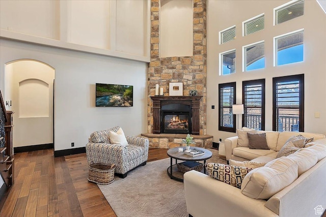 living area featuring arched walkways, a fireplace, a towering ceiling, and dark wood-style flooring