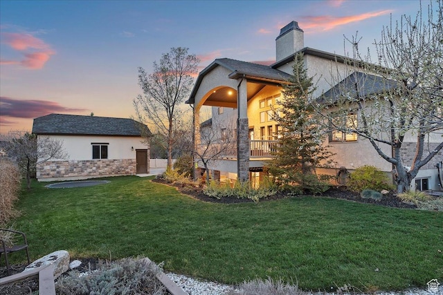 exterior space featuring a yard, stucco siding, stone siding, and a chimney