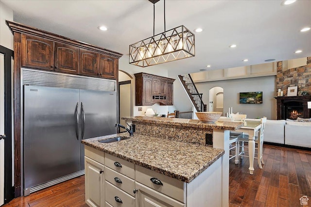 kitchen featuring dark wood-type flooring, arched walkways, stainless steel built in refrigerator, dark brown cabinets, and a sink