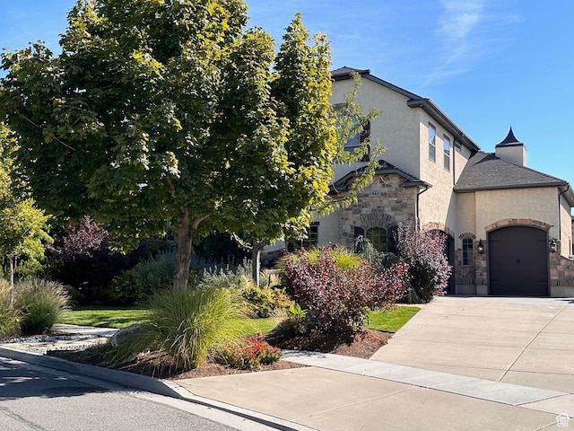 view of front of property with an attached garage, driveway, stone siding, and stucco siding