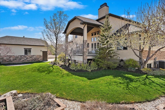 rear view of house featuring a yard, a chimney, central AC, and stucco siding