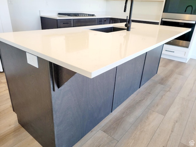 kitchen with gas stovetop, a sink, light countertops, light wood-style flooring, and an island with sink