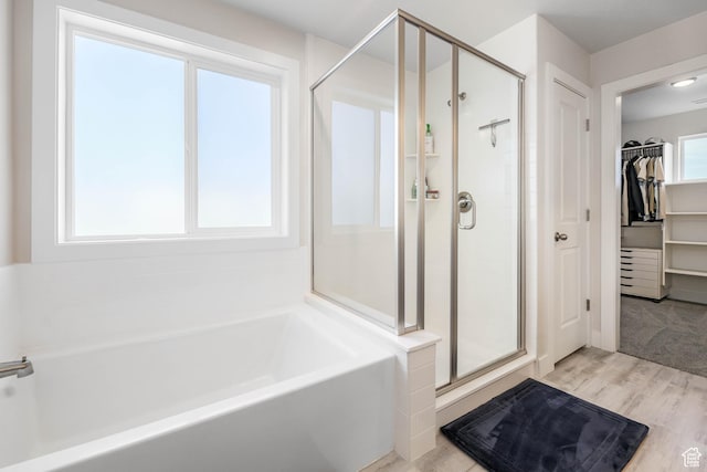 full bathroom with a walk in closet, a bath, a shower stall, and wood finished floors